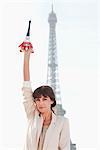 Woman holding a replica of the Eiffel Tower in front of the original one, Paris, Ile-de-France, France