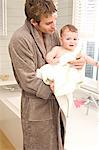 Young man in bathrobe with baby in bathroom