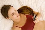 Portrait of a young woman lying on a bed, holding her cell