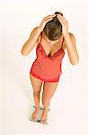 High angle view of a young woman standing on a bathroom scale with her hands on her head