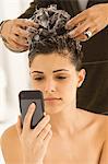 Woman using a mobile phone and having hair washed by a hairdresser