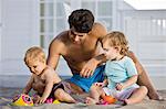 Man playing with his son and daughter in sand