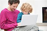 Close-up of a man assisting his son in using a laptop