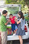 Smiling parents lifting little girl against car