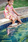 Girl sitting at edge of swimming pool with toy boat in water