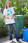 Portrait of a woman holding water bottles in hand beside recycling bin