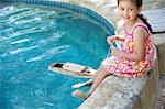 Girl sitting at edge of swimming pool with toy boat in water