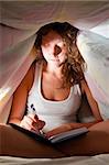 woman is sitting under cover in bed and writing her diary