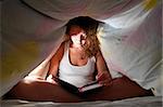 woman is reading under cover in bed and writing her diary