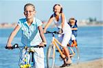 Cute girl with her mother and brother ride bikes along the beach. Focus on girl