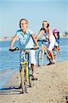 Cute girl with her mother and brother ride bikes along the beach. Focus on girl. Vertical view