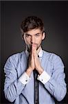 Handsome young business man standing praying, black background