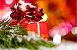 red gift box on snow with christmas tree branch on blurred background