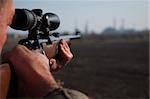 Hunter aiming with sniper rifle in the field