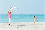 Young cute girl playing her brother with a colorful kite on the tropical beach.