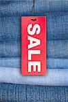 Red Sale Sign With Stack of Blue Jeans in Background