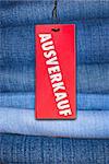 Red German Sale Sign With Stack of Blue Jeans in Background