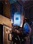 Manual worker in steel factory using welding mask, tools and machinery on metal. Vertical shape, side view, waist up