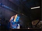 Manual worker in steel factory using welding mask, tools and machinery on metal. Horizontal shape, side view, waist up