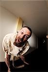 Photo of an insane man in his forties wearing a straitjacket standing in the hallway of an asylum.  Taken with a fisheye lens.