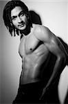 Portrait shot of a shirtless attractive young Indian man with long hair posing with hand on hip.