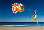 Beautiful and athletic girl with colorful balloons jumping on the beach