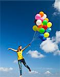 Happy young woman holding colorful balloons and flying over a green meadow