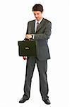 Full length portrait of modern businessman with suitcase looking on watch