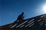 Carpenter working on top of the roof wooden structure - strong backlight silhouette