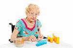 Senior woman in a wheelchair, couting out her pills for the week.  White background.