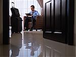 Mid adult caucasian manager typing on tablet pc in hotel room during business travel. Low angle view, full length