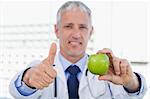 Doctor showing an apple with the thumb up in his office