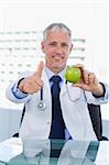 Portrait of a doctor showing an apple with the thumb up in his office