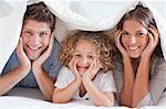 Family posing under a duvet while looking at the camera
