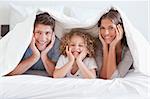 Happy family posing under a duvet while looking at the camera