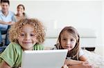 Smiling children using a tablet computer while their happy parents are watching in their living room