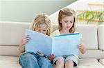 Siblings reading magazine together on the sofa