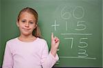 Cute schoolgirl raising her hand in front of a blackboard