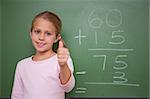 Cute schoolgirl with the thumb up in front of a blackboard