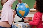 Cute little schoolgirls looking at a globe in a classroom