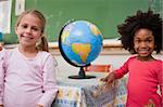 Cute schoolgirls posing with a globe in a classroom