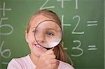 Schoolgirl looking through a magnifying glass against a blackboard