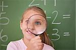 Playful schoolgirl looking through a magnifying glass in a classroom