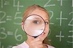 Cute schoolgirl looking through a magnifying glass in a classroom