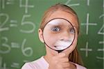 Happy schoolgirl looking through a magnifying glass in a classroom