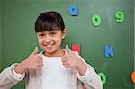 Happy schoolgirl with the thumbs up in front of a blackboard