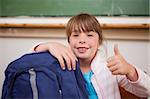 Smiling schoolgirl posing with a bag and the thumb up in a classroom