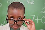 Schoolboy looking over his glasses in front of a blackboard