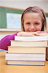 Portrait of a smiling schoolgirl posing with a stack of books in a classroom