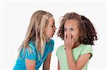 Girl whispering a secret to her friend against a white background